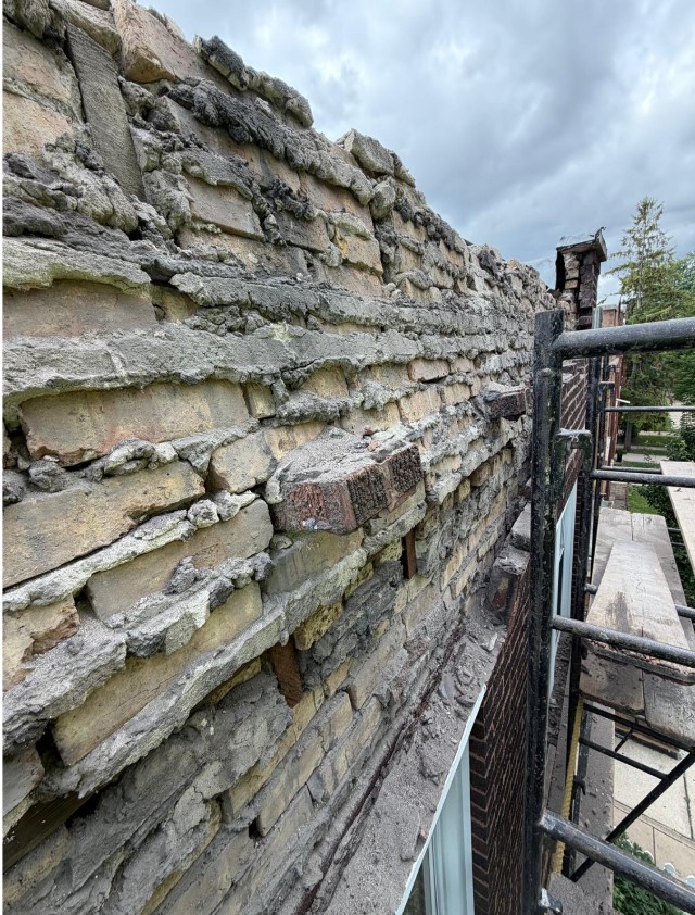 Close view of a brick parapet with badly eroded mortar joints and crumbling brick, seen from the scaffold platform