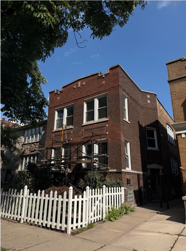 Two-story Chicago red-brick residence with a decorative brick cornice and scaffolding set up across the front of the building for masonry work