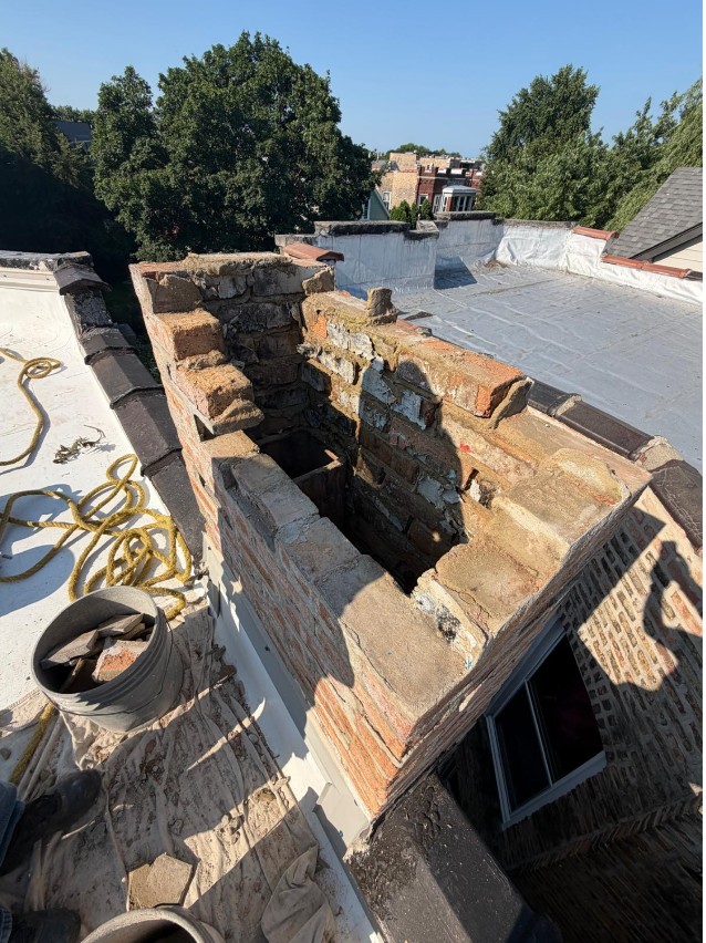 Brick chimney opened up mid-rebuild on a flat white roof, with the flue opening exposed and old brick stacked alongside