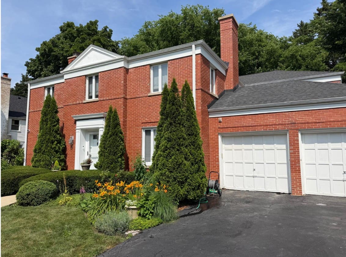 Red-brick colonial house in a leafy suburban neighborhood, with a tall brick chimney rising beside the attached garage and no equipment left on site