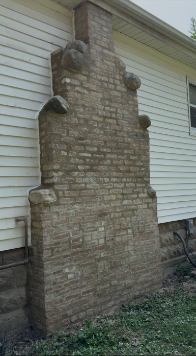 Freestanding brick chimney stack with stone accents built against the sided wall of a house