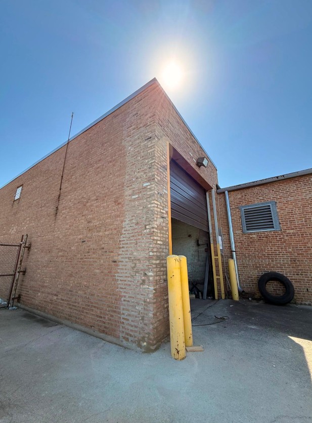 Commercial brick building with a large overhead door, yellow bollards and a sunlit brick facade