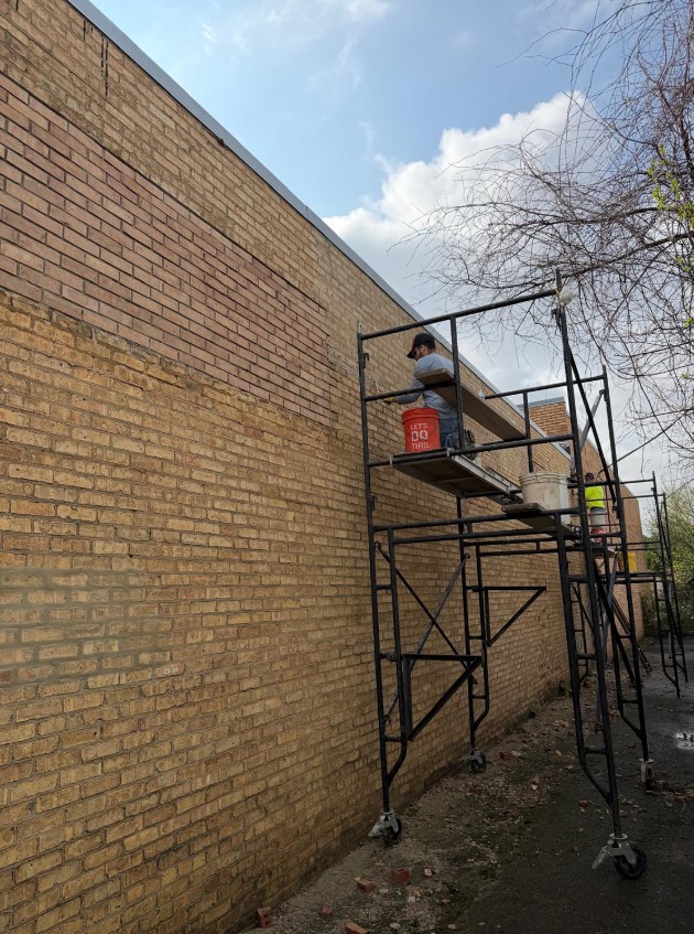Crew member working from a rolling scaffold along a long commercial brick wall